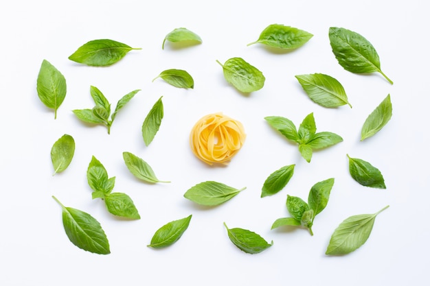 Raw tagliatelle pasta with basil leaves on white