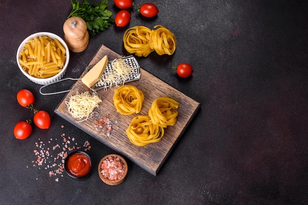 Raw tagliatelle paste with grated cheese cherry tomatoes spices and herbs on a wooden cutting board