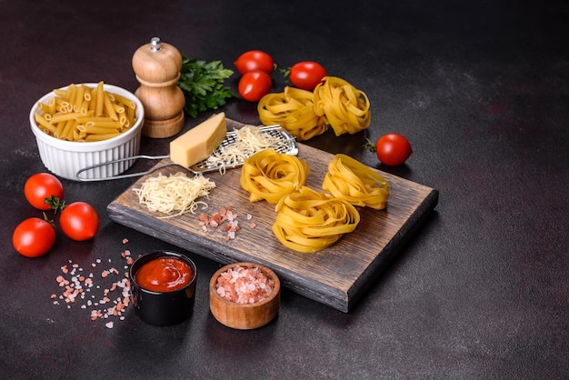 Raw tagliatelle paste with grated cheese cherry tomatoes spices and herbs on a wooden cutting board