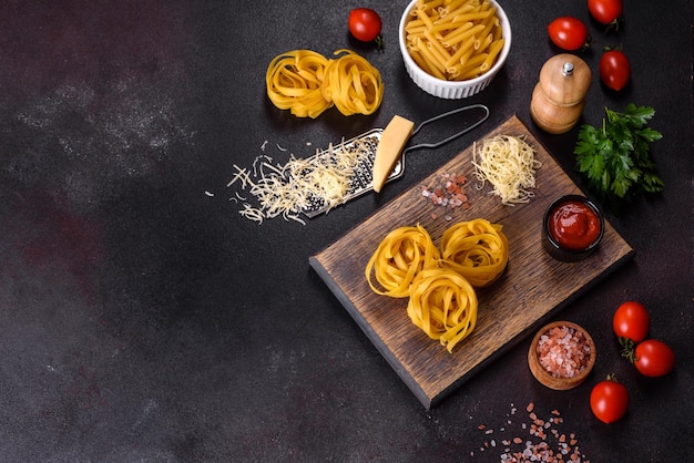 Pasta di tagliatelle crude con formaggio grattugiato pomodorini spezie ed erbe aromatiche su un tagliere di legno