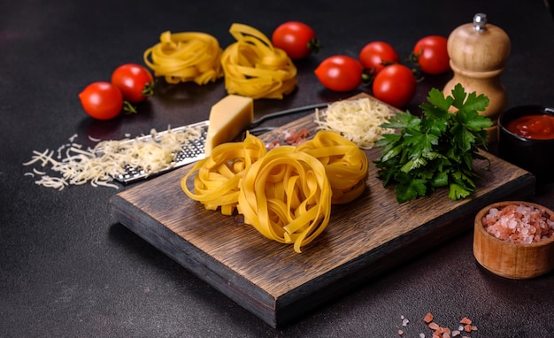 Raw tagliatelle paste with grated cheese cherry tomatoes spices and herbs on a wooden cutting board