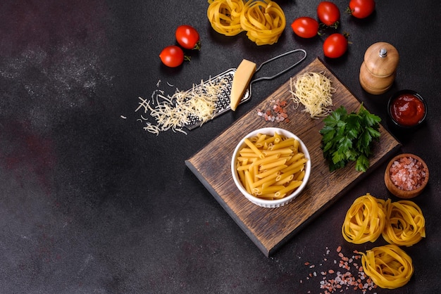 Pasta di tagliatelle crude con formaggio grattugiato pomodorini spezie ed erbe aromatiche su un tagliere di legno