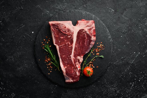 Raw tbone steak on a stone table with thyme rosemary and spices\
top view flat lay top view on black stone cutting table