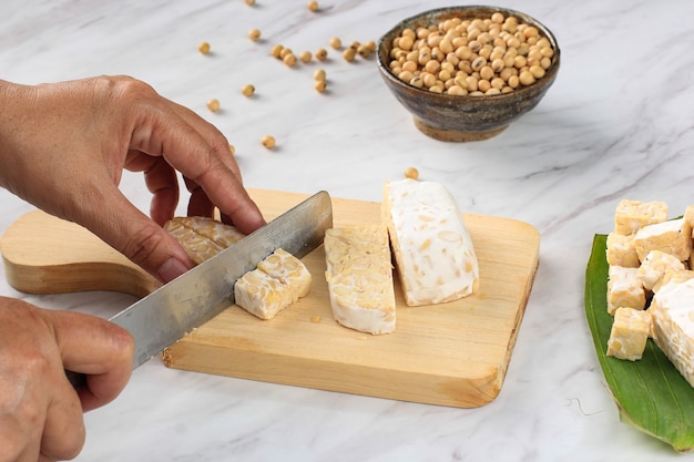 Raw Tempeh or Tempe. Tempeh Slices on Wooden Background, Cut by Asian Female Chef. Tempe Made From Fermented Soybeans Cut by Asian Female Hand