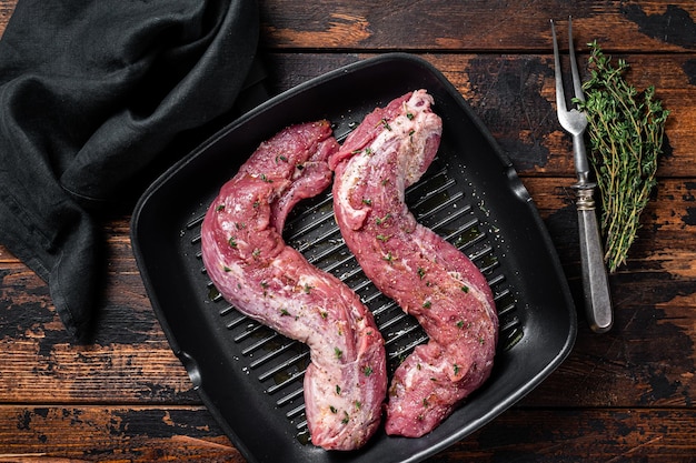 Raw Tenderloin pork fillet ready for cooking uncooked meat in grill pan with herbs and olive oil Wooden background Top view