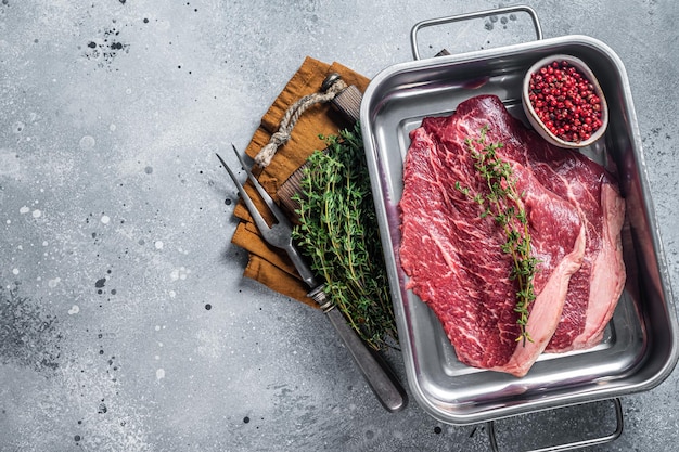 Raw thin marbled beef steak with spices in kitchen tray. Gray background. Top view. Copy space.