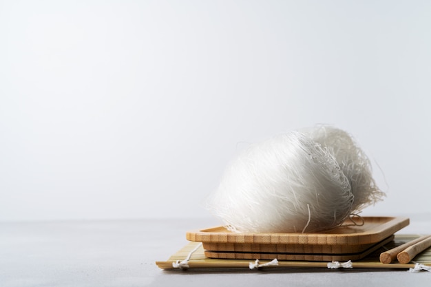 Raw thin rice noodles on bamboo dish with chopsticks on stone surface with copy space.