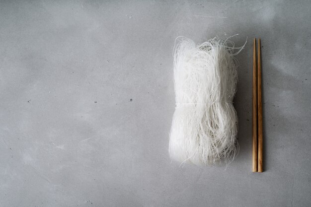 Raw thin rice noodles on stone surface with chopsticks. 