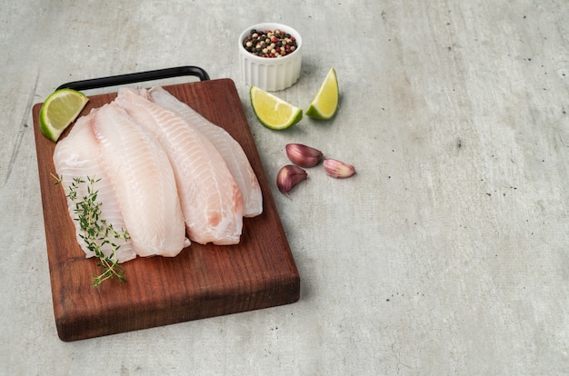 Raw tilapia fish fillet with seasonings over wooden board.