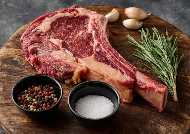 Bistecca di manzo tomahawk cruda con ingredienti per grigliare rosmarino sale pepe e aglio primo piano