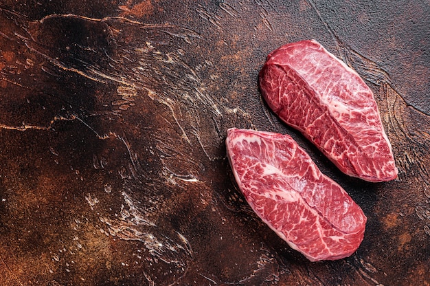 Raw Top Blade or flat iron beef meat steaks on a butcher table. Dark background. Top View. Copy space.