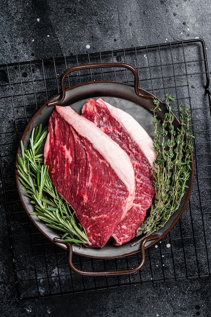 Raw top sirloin or picanha beef meat steak in a steel tray\
black wooden background top view