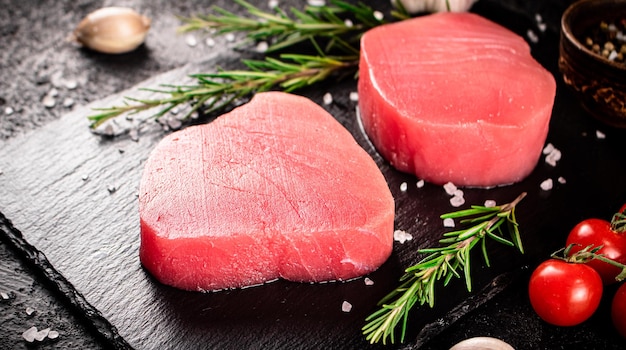 raw tuna steak on a stone board with rosemary spices and tomatoes