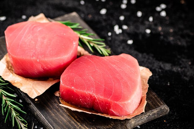 Photo raw tuna steaks on a rosemary cutting board