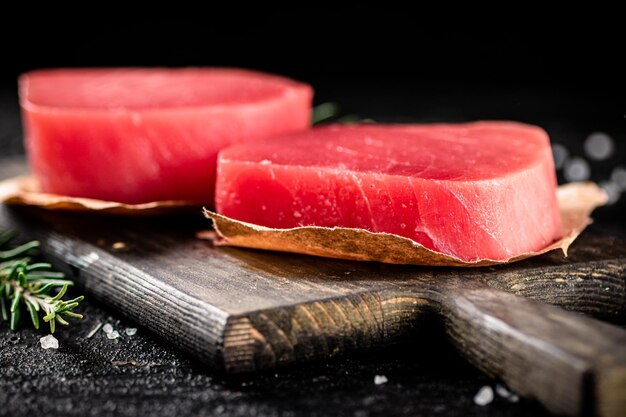 Сырые стейки из тунца на разделочной доске с розмарином