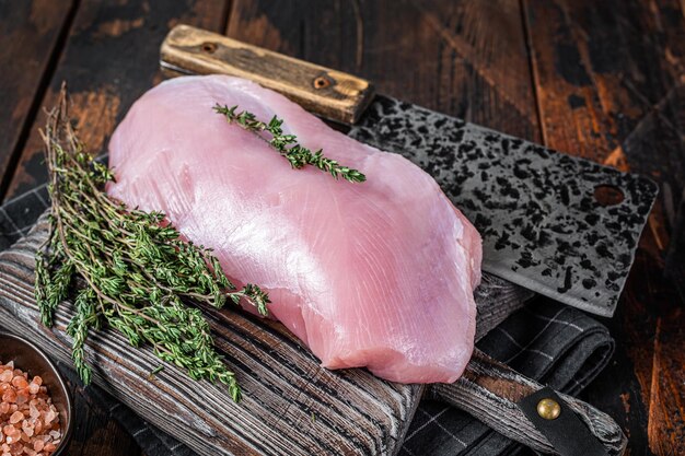 肉切り包丁が付いている木の肉屋の板の生の七面鳥の胸の切り身。暗い木の背景。上面図。