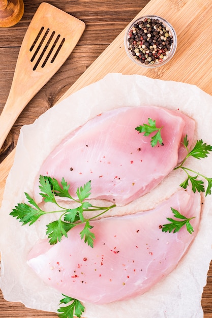 Raw turkey fillet in spices and herbs on a cutting board on a wooden table.