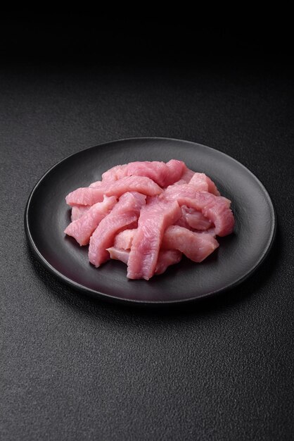 Raw turkey meat in the form of slices with salt spices and herbs on a dark concrete background