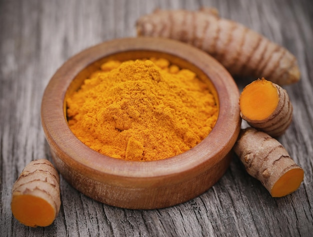 Raw turmeric with powder in a bowl on wooden surface