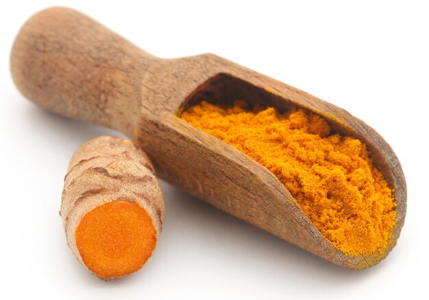 Raw turmeric with powder in wooden scoop over white background