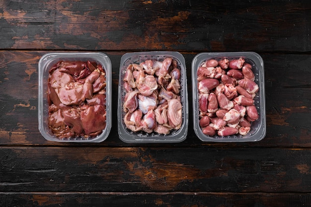 Raw uncooked Bird chicken giblets gizzards, stomachs, liver, offal, hearts set, on old dark  wooden table background, top view flat lay, with copy space for text