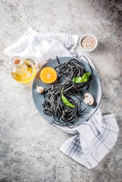 Raw uncooked black cuttlefish ink spaghetti pasta with ingredients for cooking dinner on grey stone table 