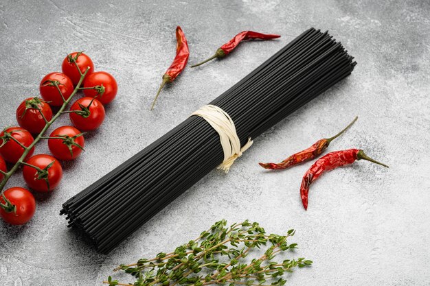 Raw uncooked black cuttlefish ink spaghetti set, on gray stone table background