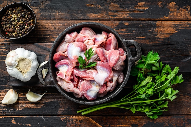 Raw uncooked chicken gizzards, stomach in a pan. Dark wooden background. Top view.