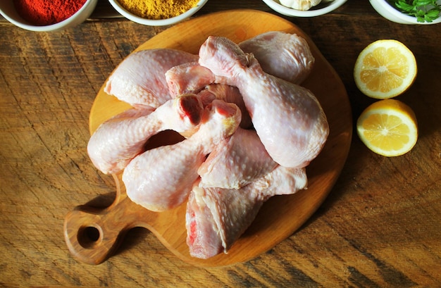 Raw uncooked chicken legs drumsticks on cutting board meat with ingredients for cooking