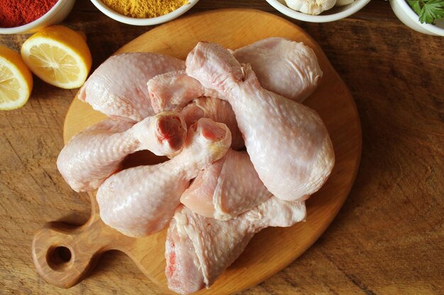 Raw uncooked chicken legs drumsticks on cutting board meat with ingredients for cooking