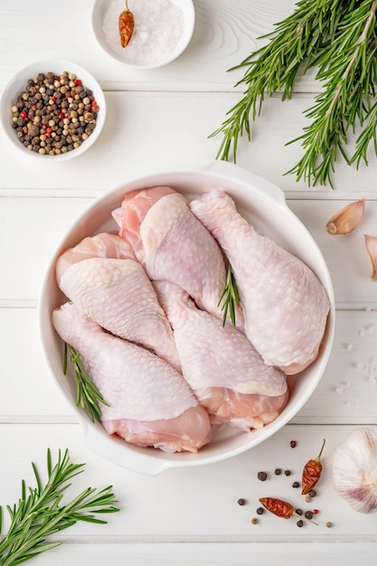 Raw uncooked chicken legs in a white dish Meat with ingredients for cooking Top view