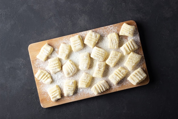 Raw uncooked homemade potato gnocchi with flour on cutting board. Top view. Dark background.