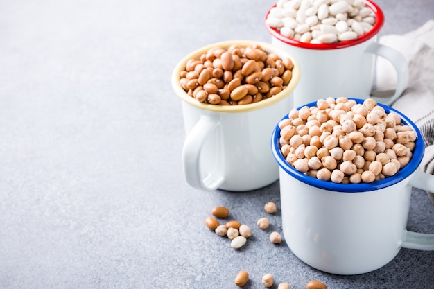 Raw uncooked organic chickpeas and kidney beans in white enamel mugs 