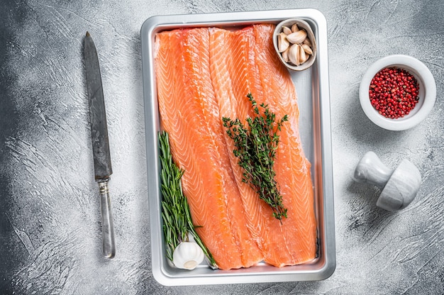 Filetto di salmone di mare crudo crudo in un vassoio da cucina con erbe aromatiche. sfondo bianco.