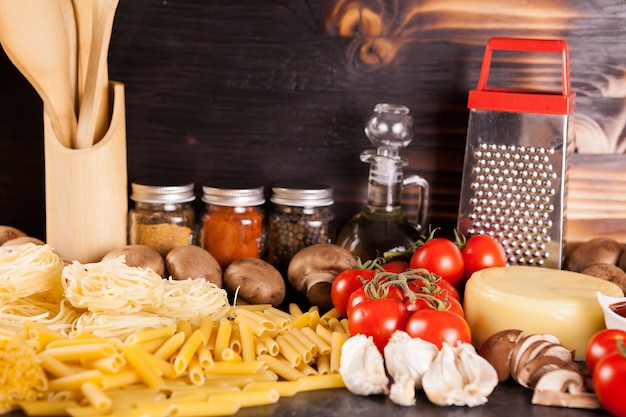 Raw uncooked spaghetti, pasta and macaroni next to fresh vegetables on rustic background