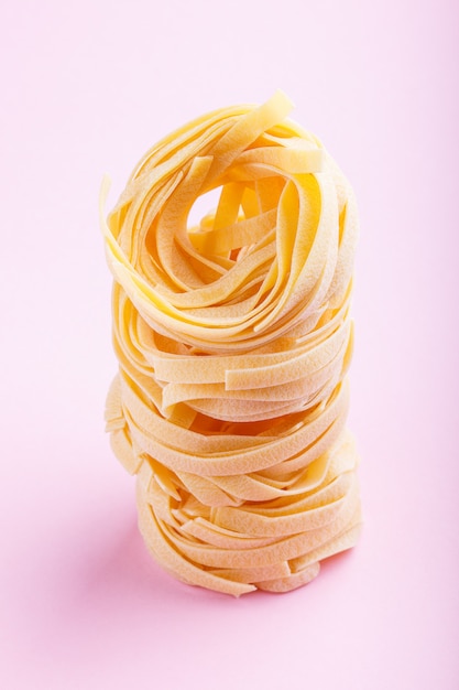 Raw uncooked tagliatelle pasta on a pink pastel background 