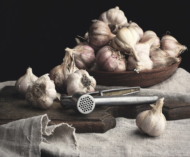 Raw unpeeled garlic on a very old vintage cutting board and iron press