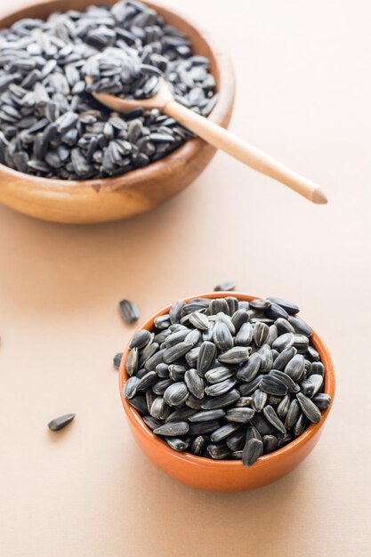 Raw unpeeled sunflower seeds in two bowls on a beige background. Natural source of vitamins and fat. Vertical view