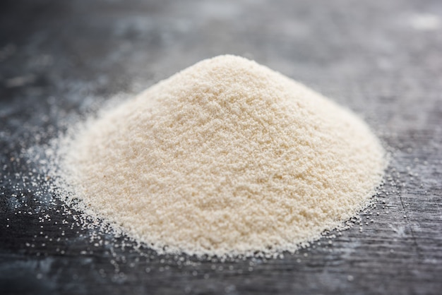 Raw unprepared semolina flour also known as Rava powder in Hindi in bowl or spoon. close-up isolated on white or moody background. selective focus