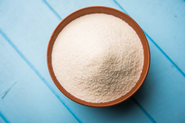 Raw unprepared semolina flour also known as Rava powder in Hindi in bowl or spoon. close-up isolated on white or moody background. selective focus