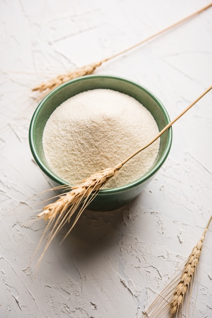 Raw unprepared semolina flour also known as Rava powder in Hindi in bowl or spoon. close-up isolated on white or moody background. selective focus