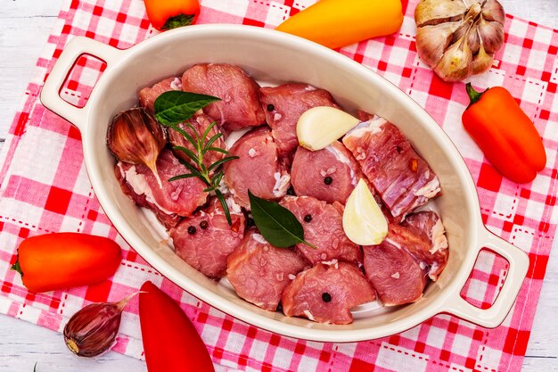 Vitello crudo tagliato a pezzi con verdure e altri ingredienti pronti da cuocere. tavolo rustico in legno bianco, concetto culinario biologico, primi piani