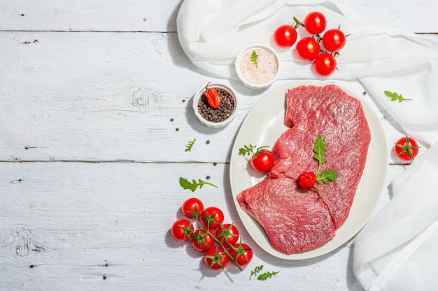 Raw veal steak with spices cherry tomatoes Trendy hard light dark shadow white wooden background
