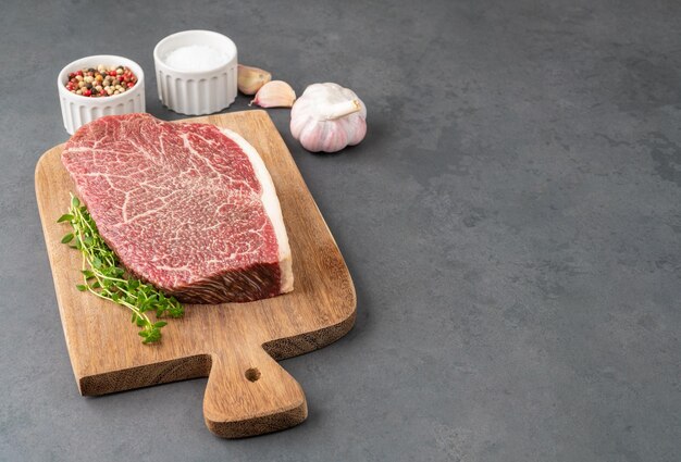 Carne cruda dell'arrosto della spalla di wagyu sopra la tavola di legno con i condimenti e lo spazio della copia