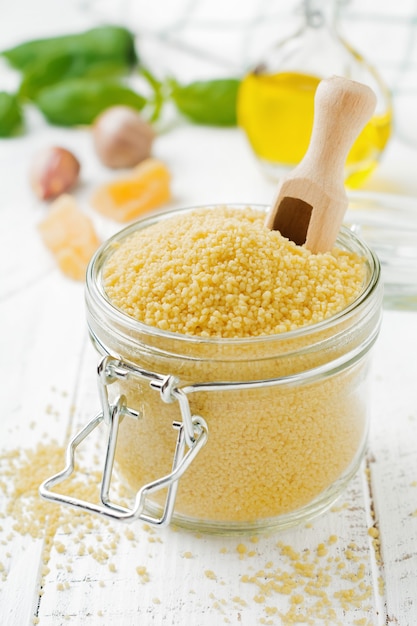 Raw wheat cereals couscous in a glass jar on a light concrete or stone background Traditional food of North Africa and southern Europe