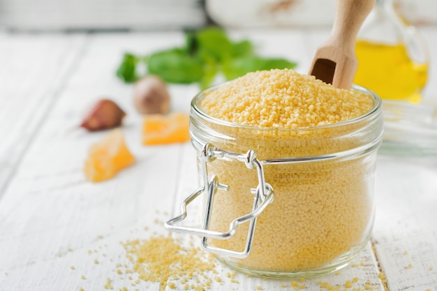 Raw wheat cereals couscous in a glass jar on a light concrete or stone background Traditional food of North Africa and southern Europe