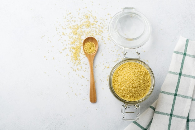 Raw wheat cereals couscous in a glass jar on a light concrete or stone. Traditional food of North Africa and southern Europe. 