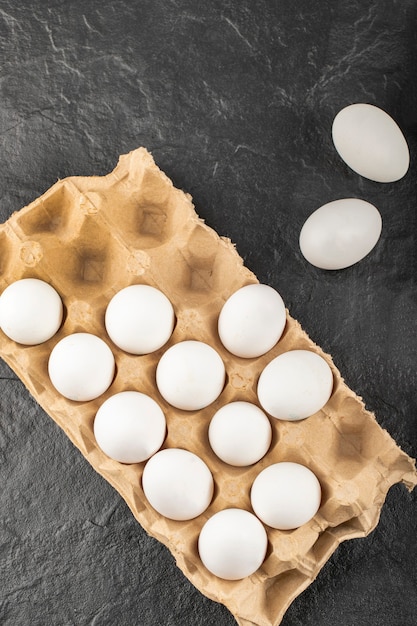 Raw white chicken eggs in a cardboard box placed on black table . 