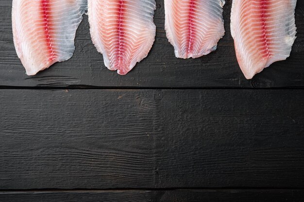 Photo raw white fish fillet cuts, on black wooden table, top view