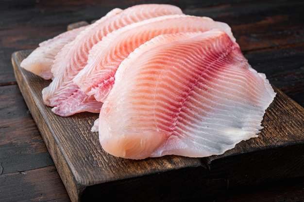 Raw white fish fillet cuts, on dark wooden table